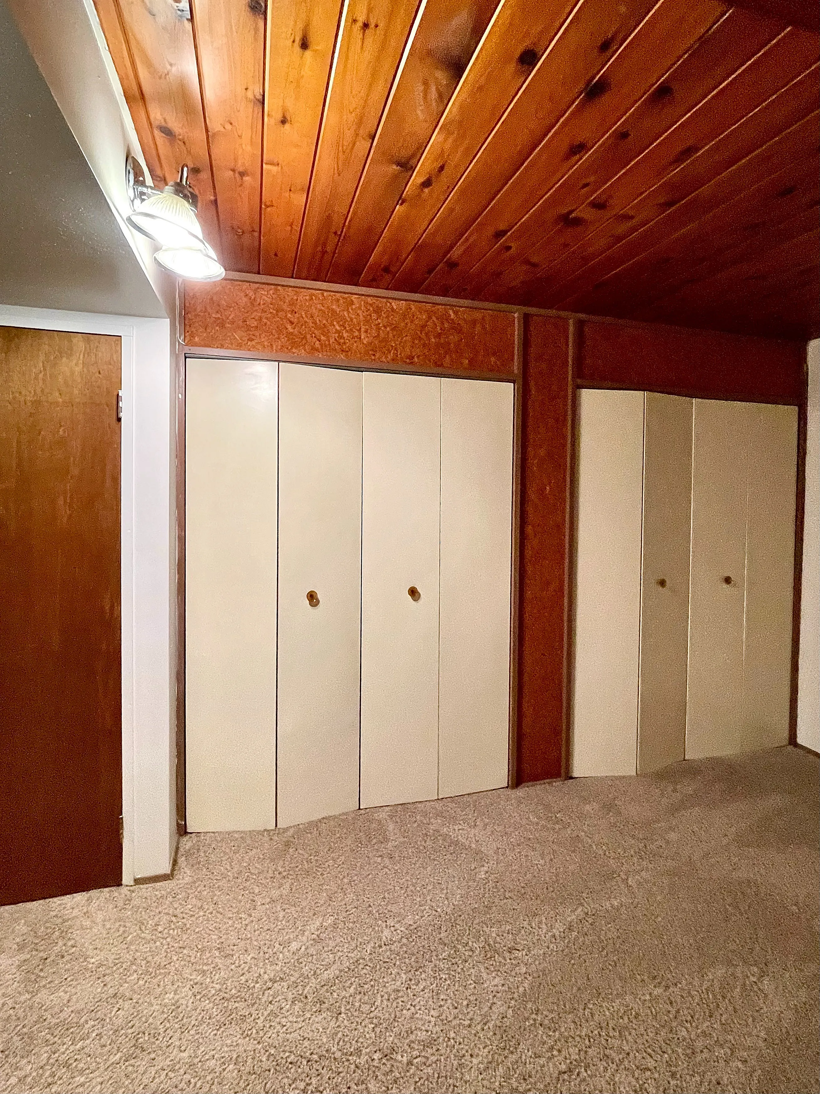 Cozy room with warm wooden ceiling, soft carpet flooring, and ample storage closets.