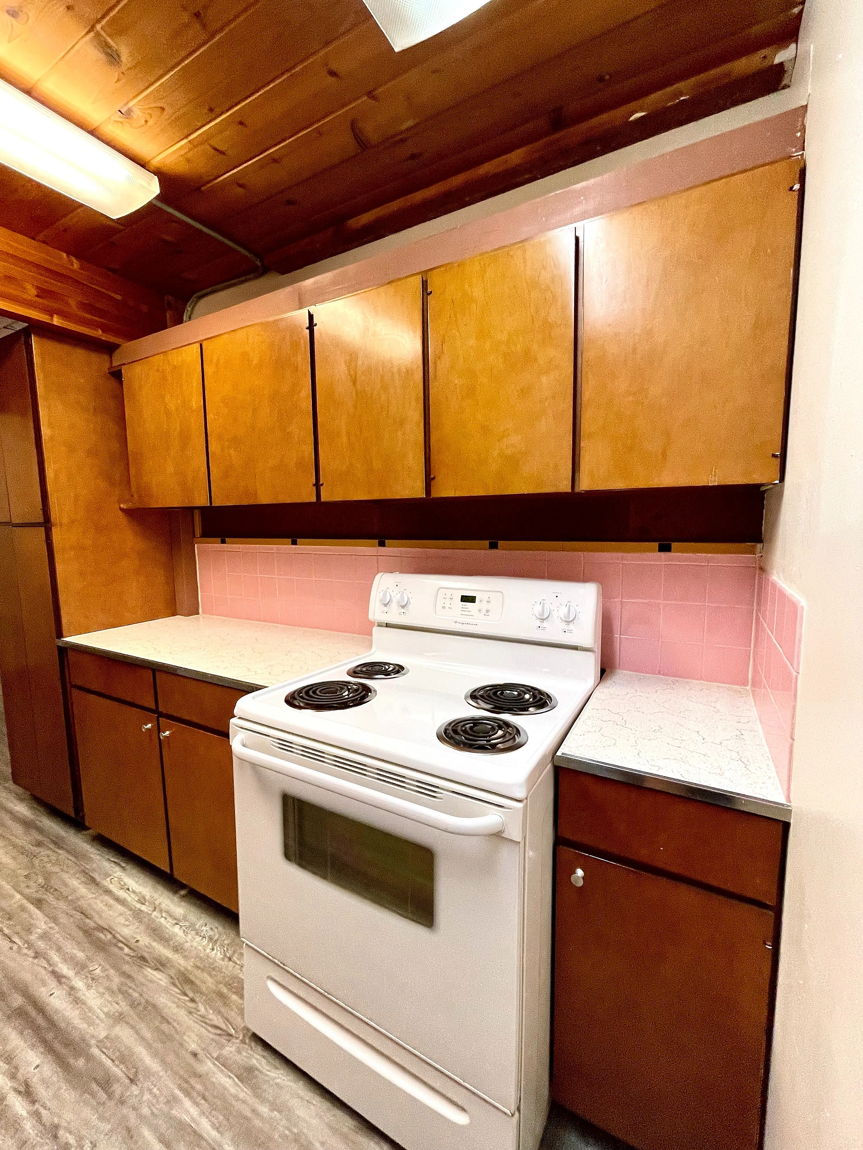 Charming kitchen with vintage wood cabinetry, pink backsplash, and modern white stove offering a cozy cooking space.