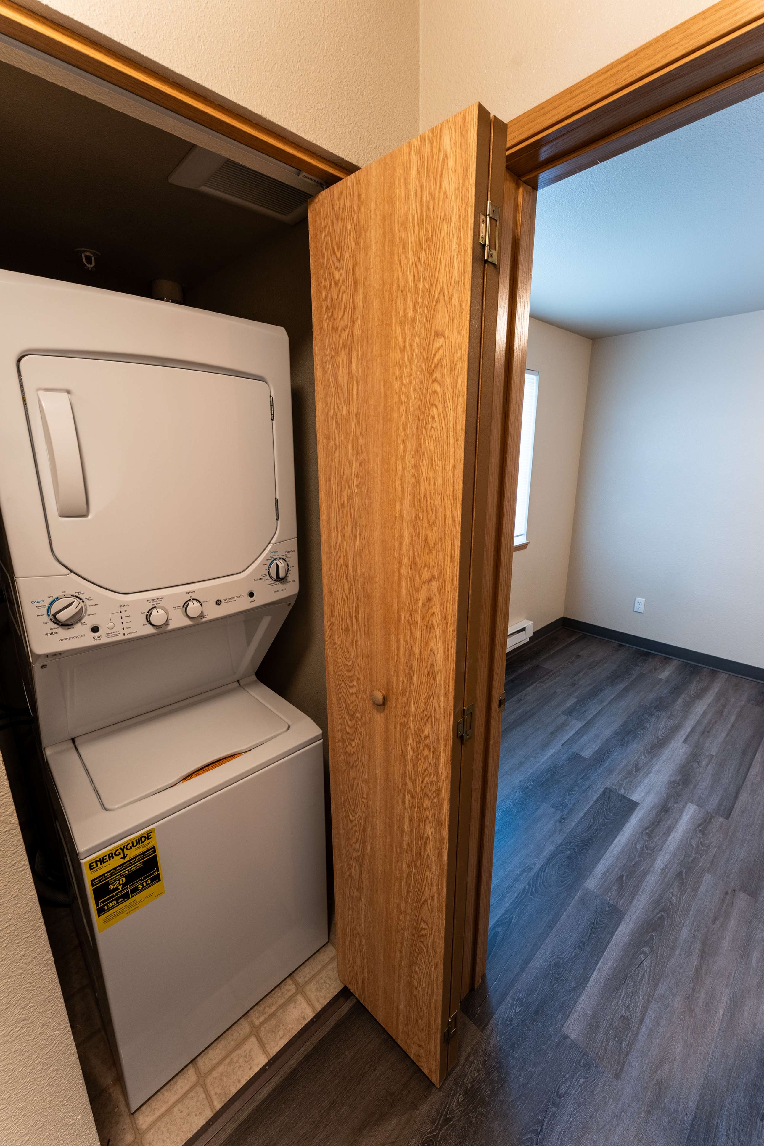 Modern apartment featuring a convenient in-unit laundry area with stackable washer and dryer, adjacent to a bright room with sleek wood-look flooring.