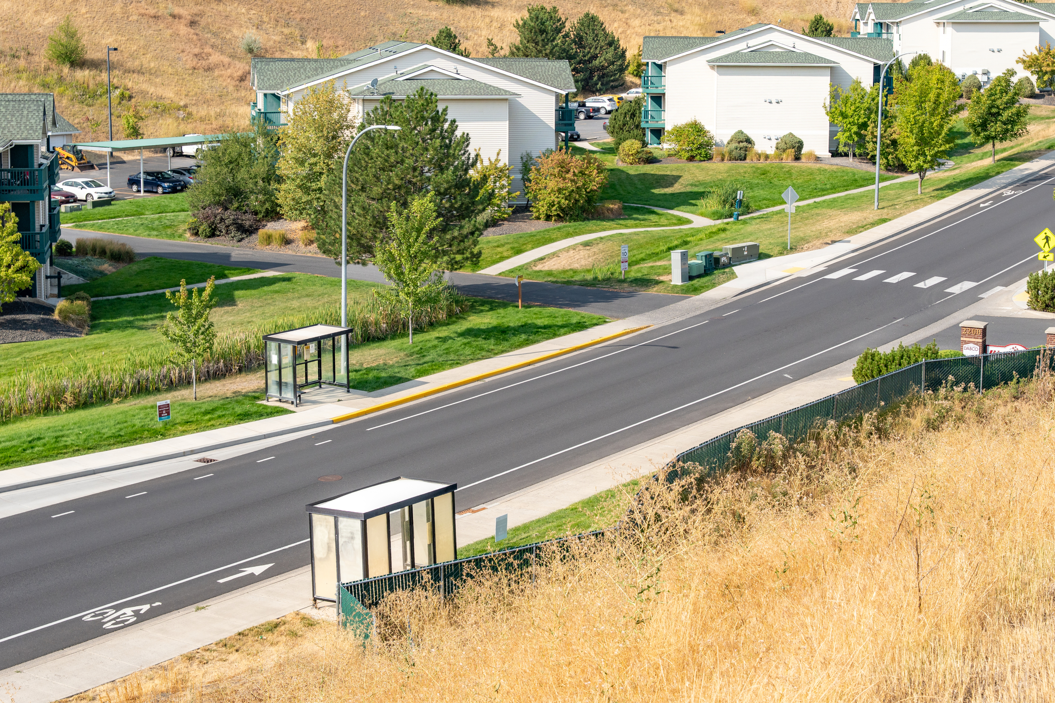 Scenic suburban street view featuring modern apartment buildings, lush greenery, and convenient bus stops for easy access.