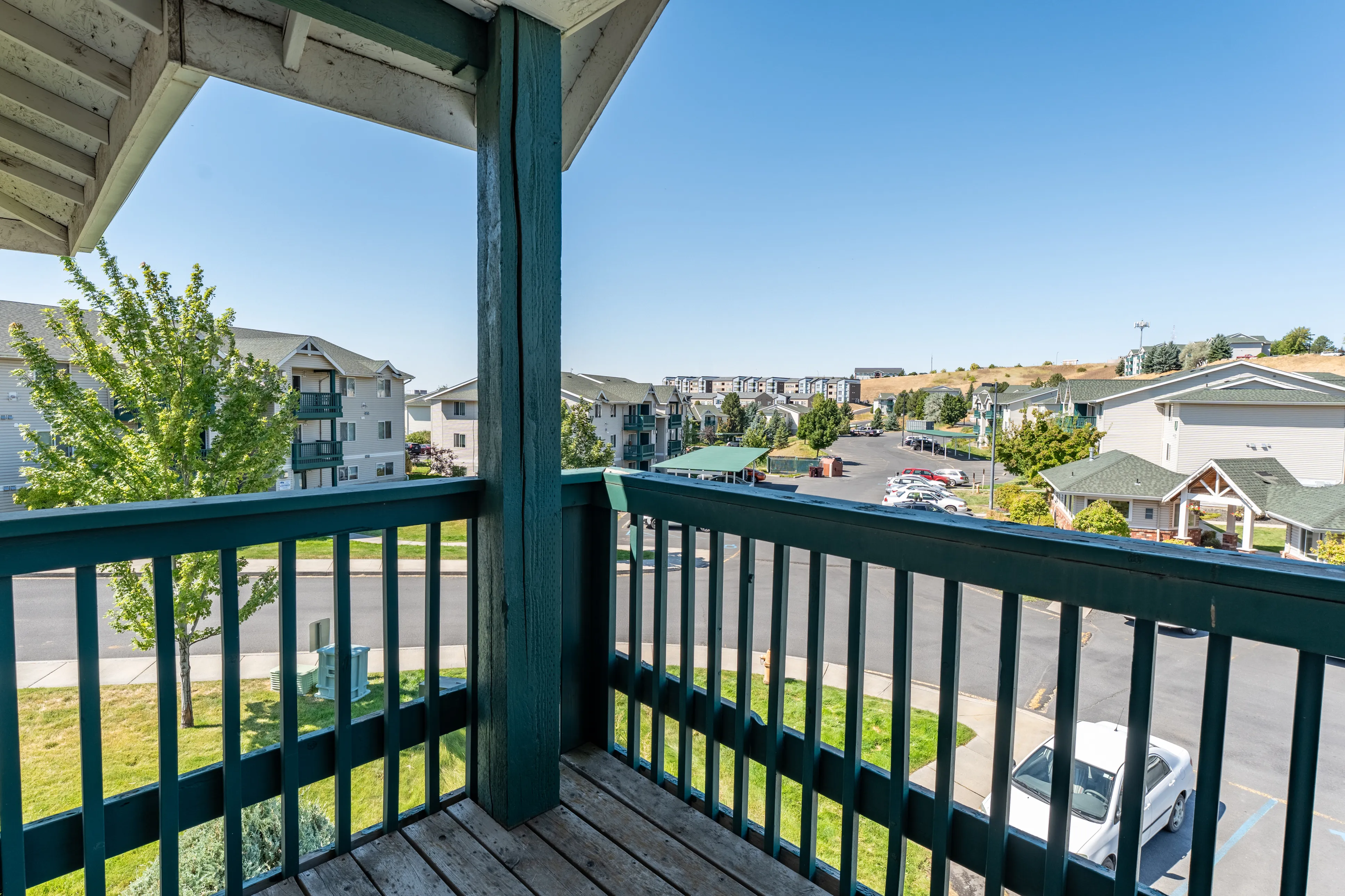 Charming apartment balcony offering serene views of a well-maintained residential complex with lush greenery and blue skies.