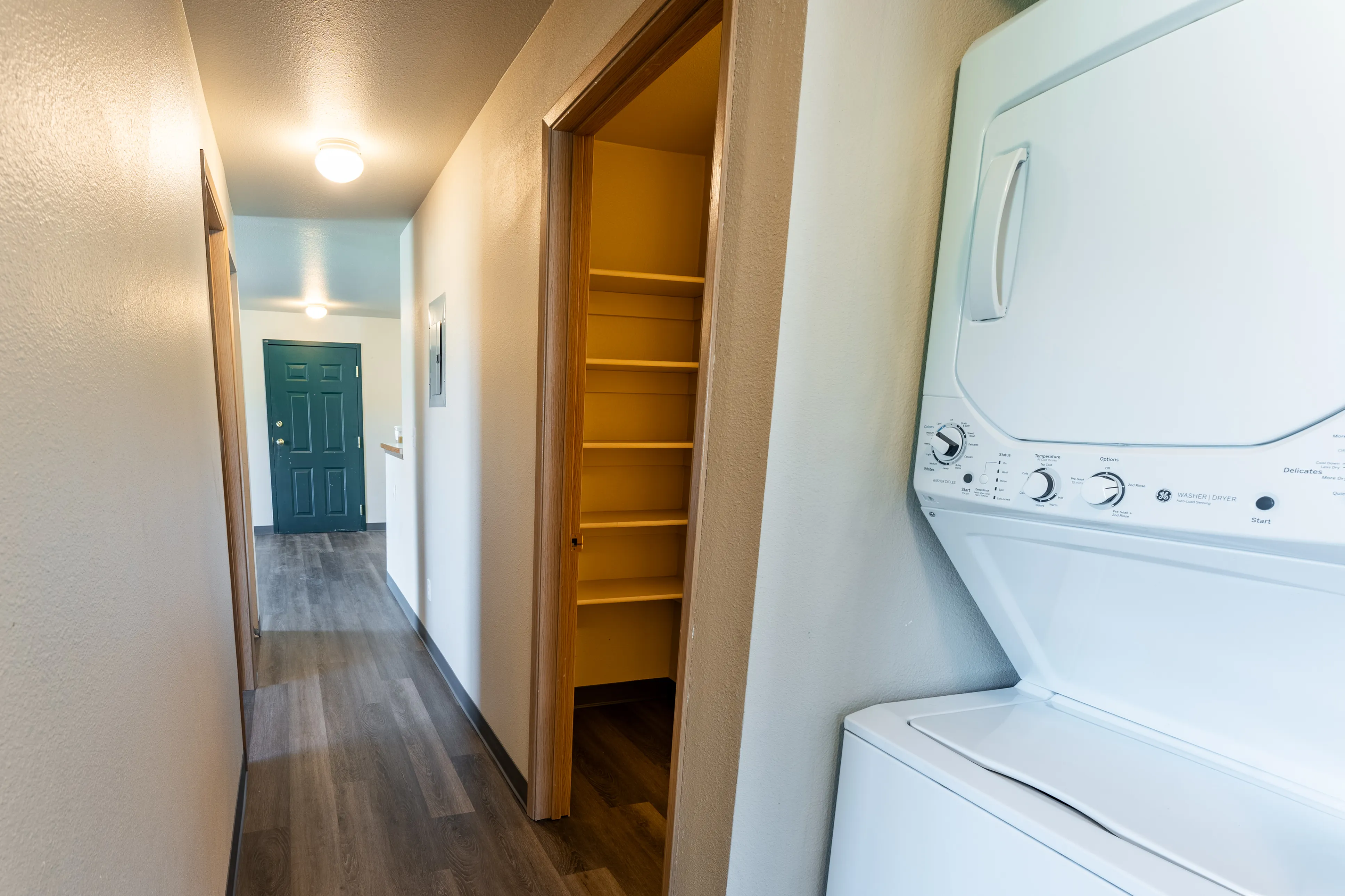 Bright hallway featuring elegant wood flooring, a convenient in-unit laundry with a washer and dryer, and ample shelving for storage.