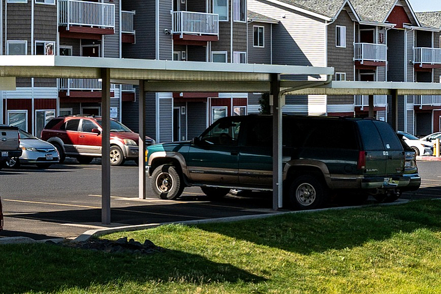 Charming suburban apartment complex with covered parking, manicured lawns, and modern architecture under a clear blue sky.