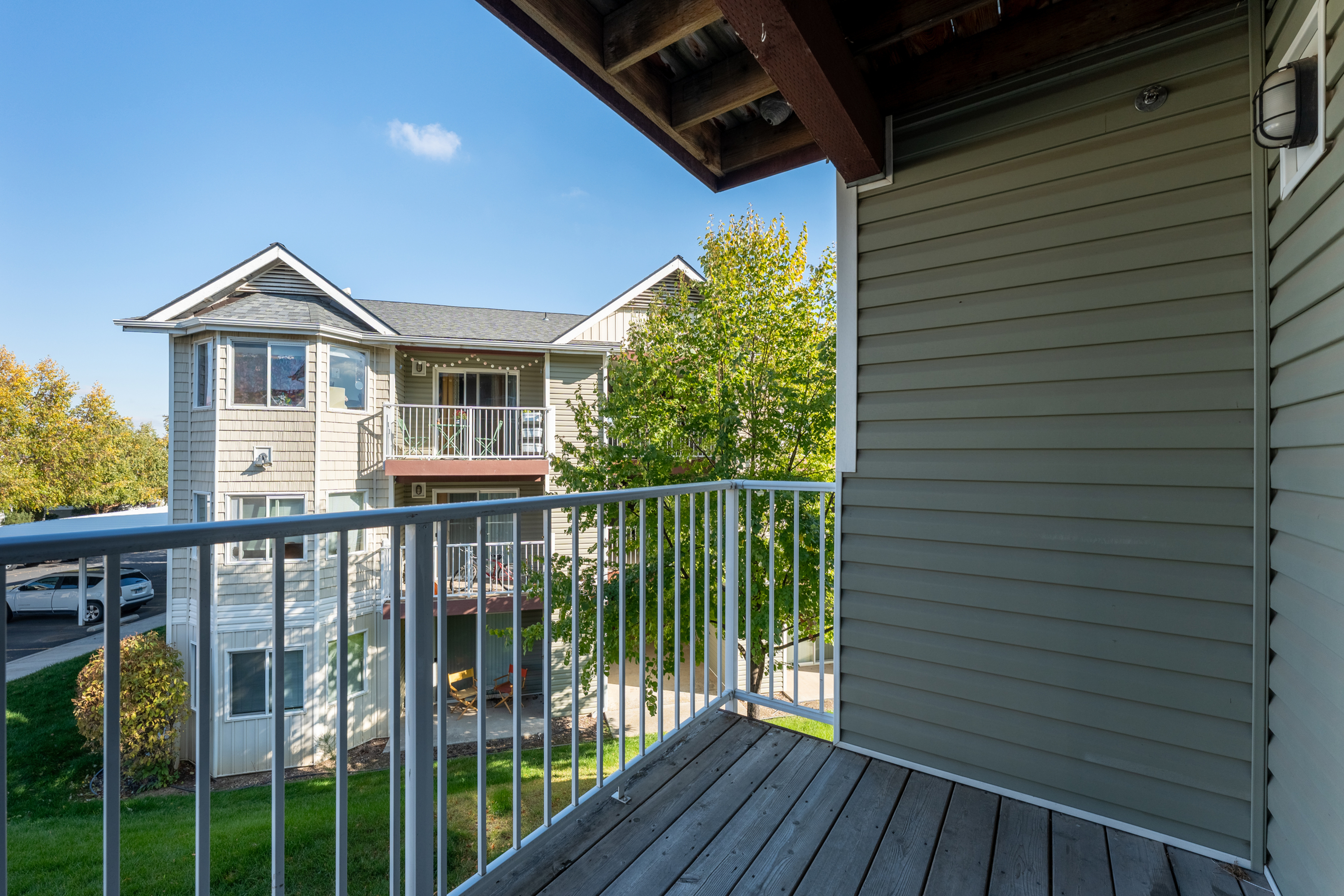 Cozy balcony with open railing, offering refreshing views of a charming apartment complex and lush greenery.