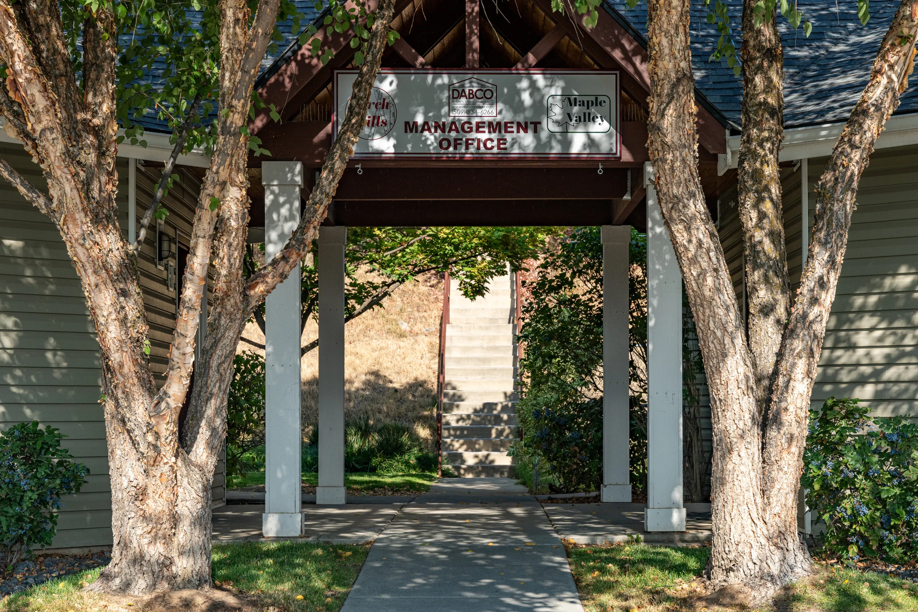 Inviting entrance to management office surrounded by lush greenery and charming architecture.