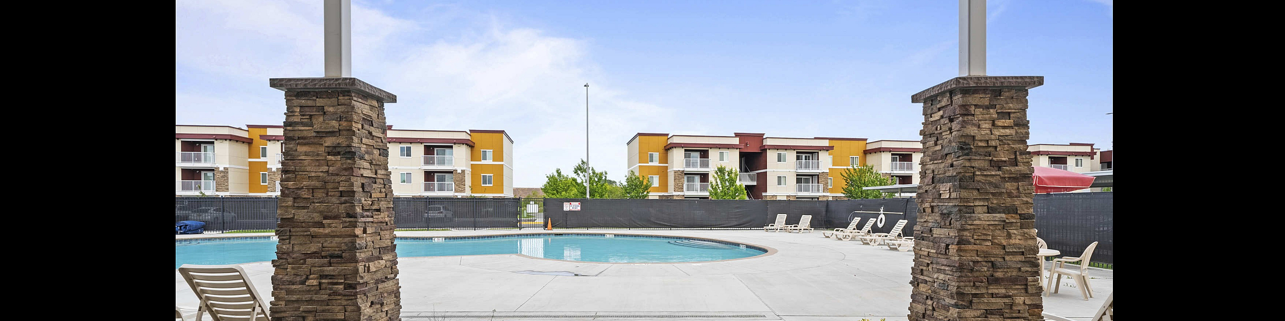 Inviting apartment complex with a serene outdoor pool area, surrounded by modern multi-story buildings and comfortable lounge chairs.