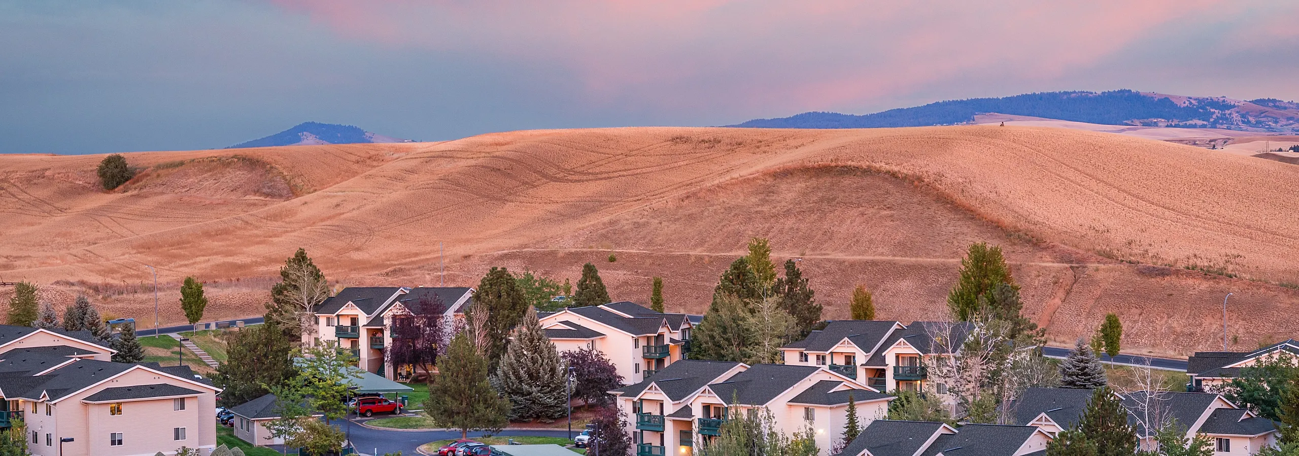Idyllic apartment community nestled against rolling hills with a breathtaking sunset sky.