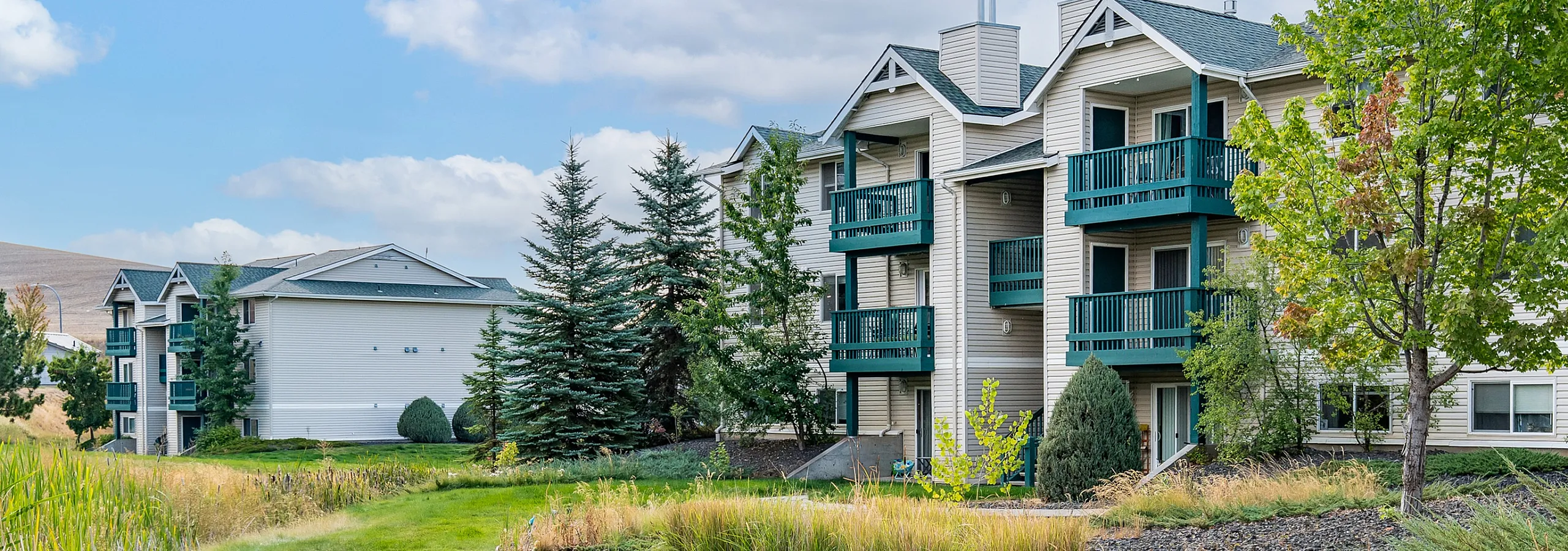 Charming apartment complex with lush green lawns, vibrant trees, and inviting balconies, offering serene suburban living.