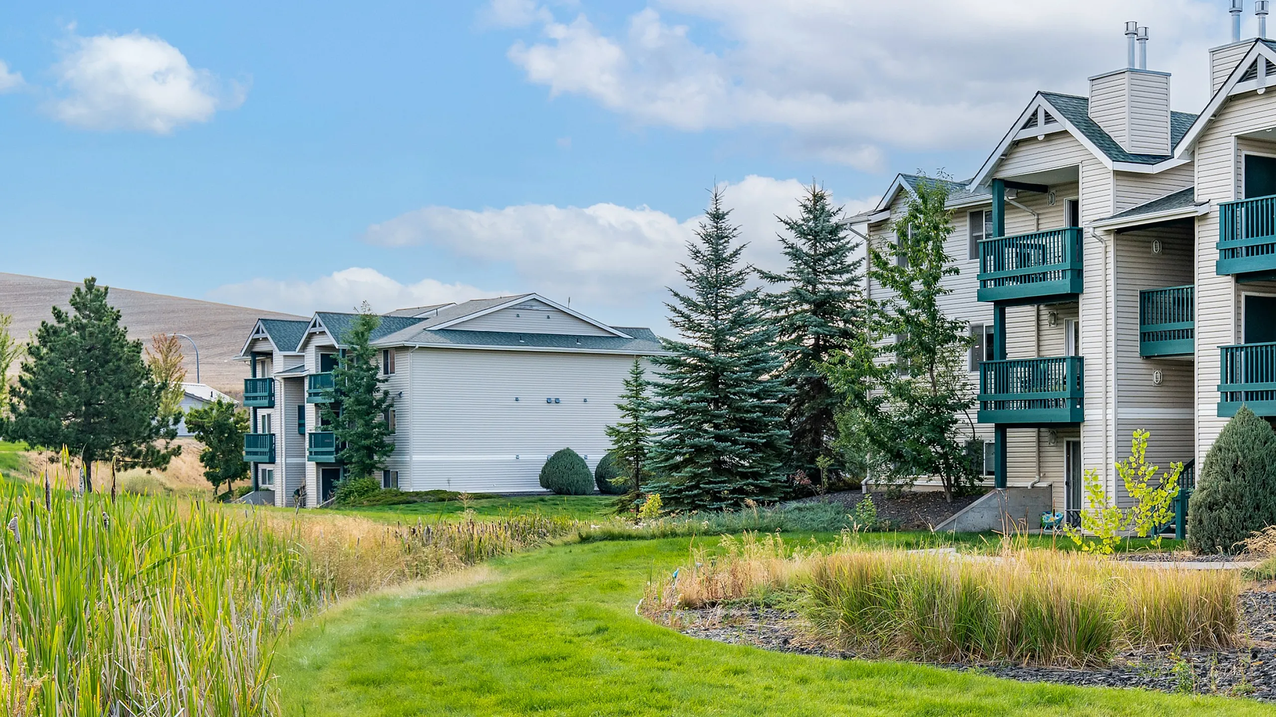 Charming apartment complex surrounded by lush greenery, featuring spacious balconies and a scenic walkway.