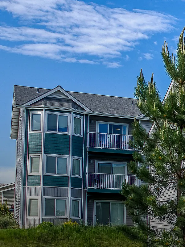 Charming apartment building with bay windows, balconies, and lush greenery set against a clear blue sky.