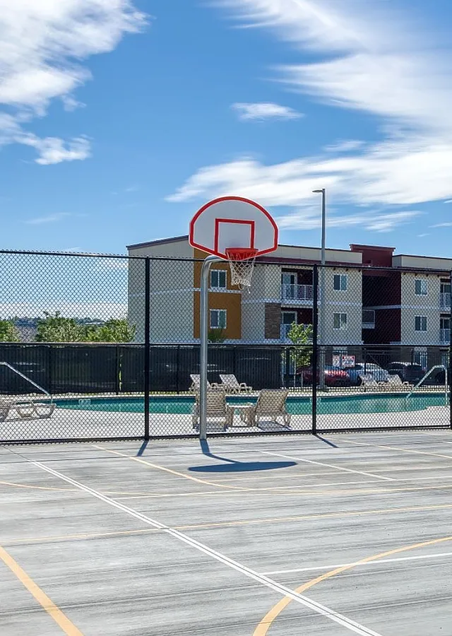 Modern outdoor basketball court with panoramic views, luxurious apartment backdrop, and clear blue skies, perfect for active living.