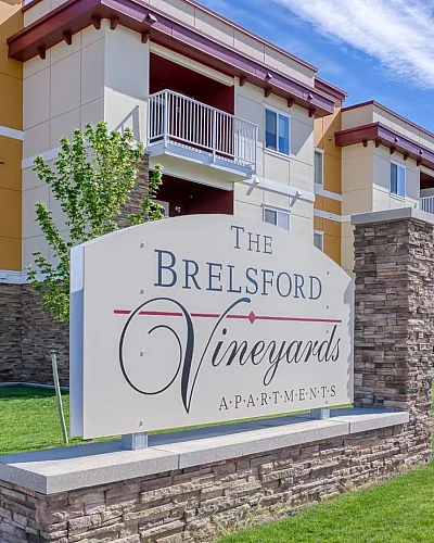 Inviting exterior view of The Brelsford Vineyards Apartments featuring modern architecture, lush landscaping, and spacious balconies under a clear blue sky.