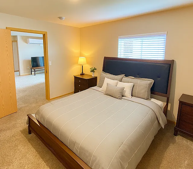 Inviting bedroom with cozy carpeting, elegant furnishings, and soft ambient lighting, perfect for restful nights in a modern apartment.