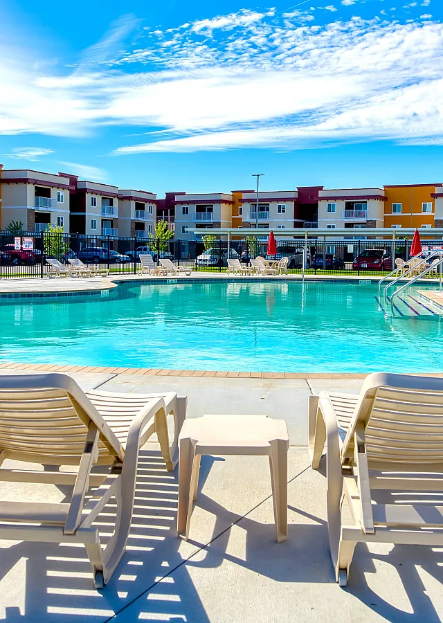 Inviting pool area with comfortable loungers and vibrant apartment complex in the background, perfect for relaxing in style.