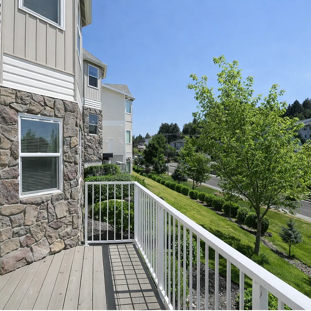 Inviting balcony with stone facade offering a serene view of lush greenery and a quiet neighborhood street.