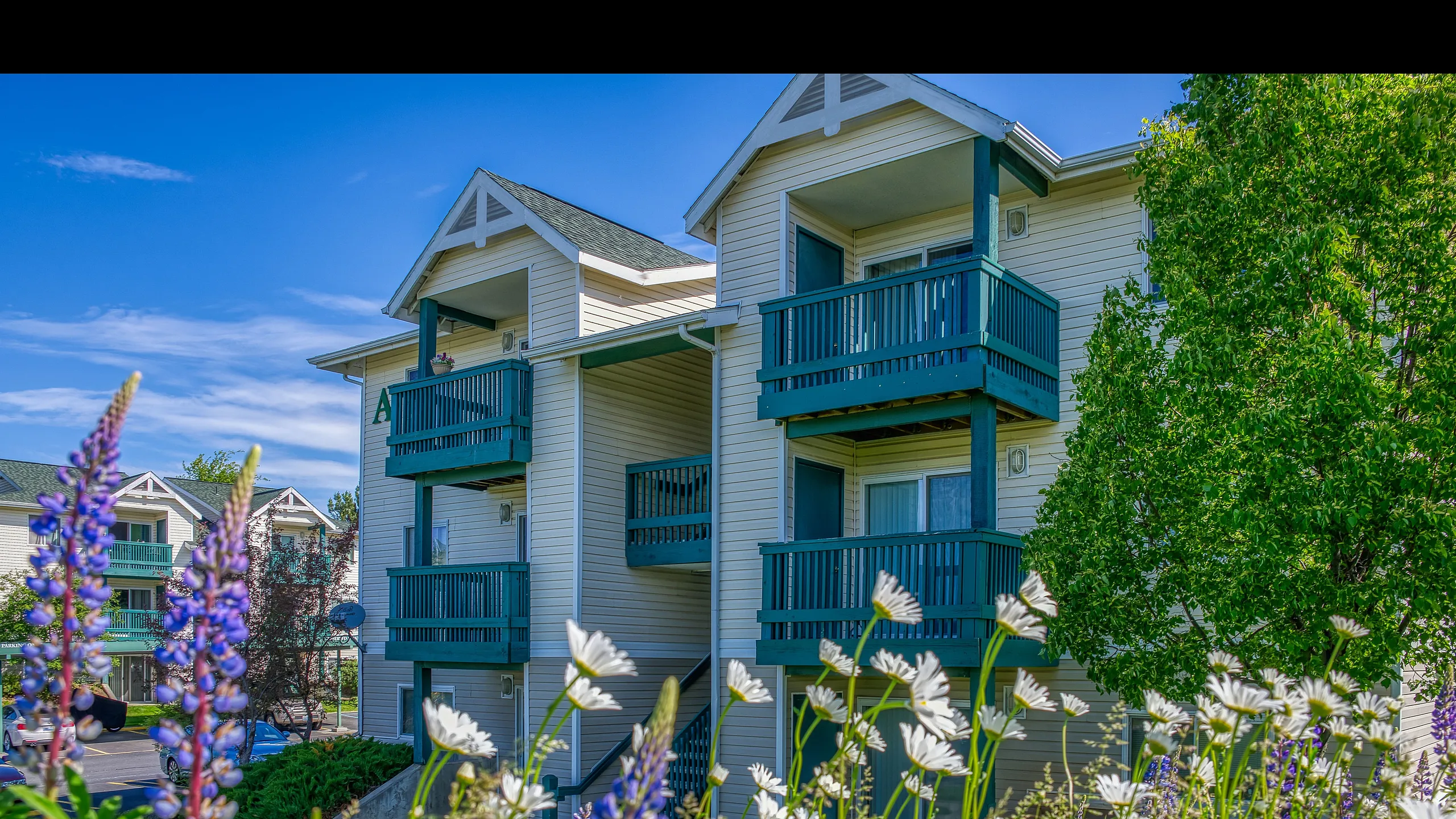 Charming apartment complex with green balconies surrounded by lush landscaping and vibrant wildflowers.