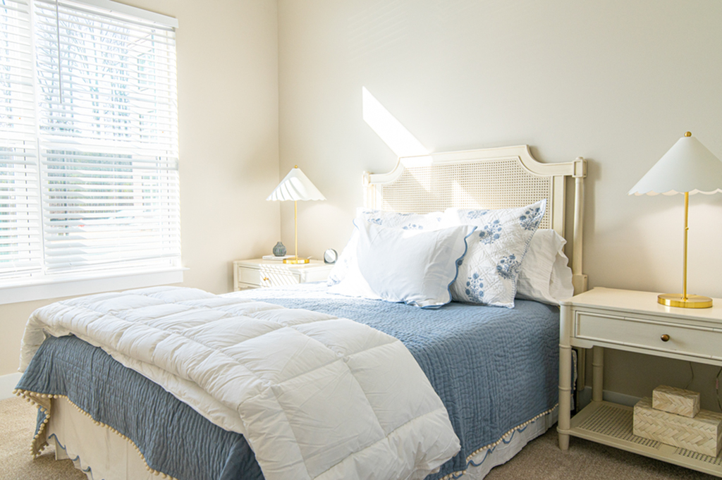 Bright and inviting bedroom with soft blue and white bedding, natural light streaming through large windows.