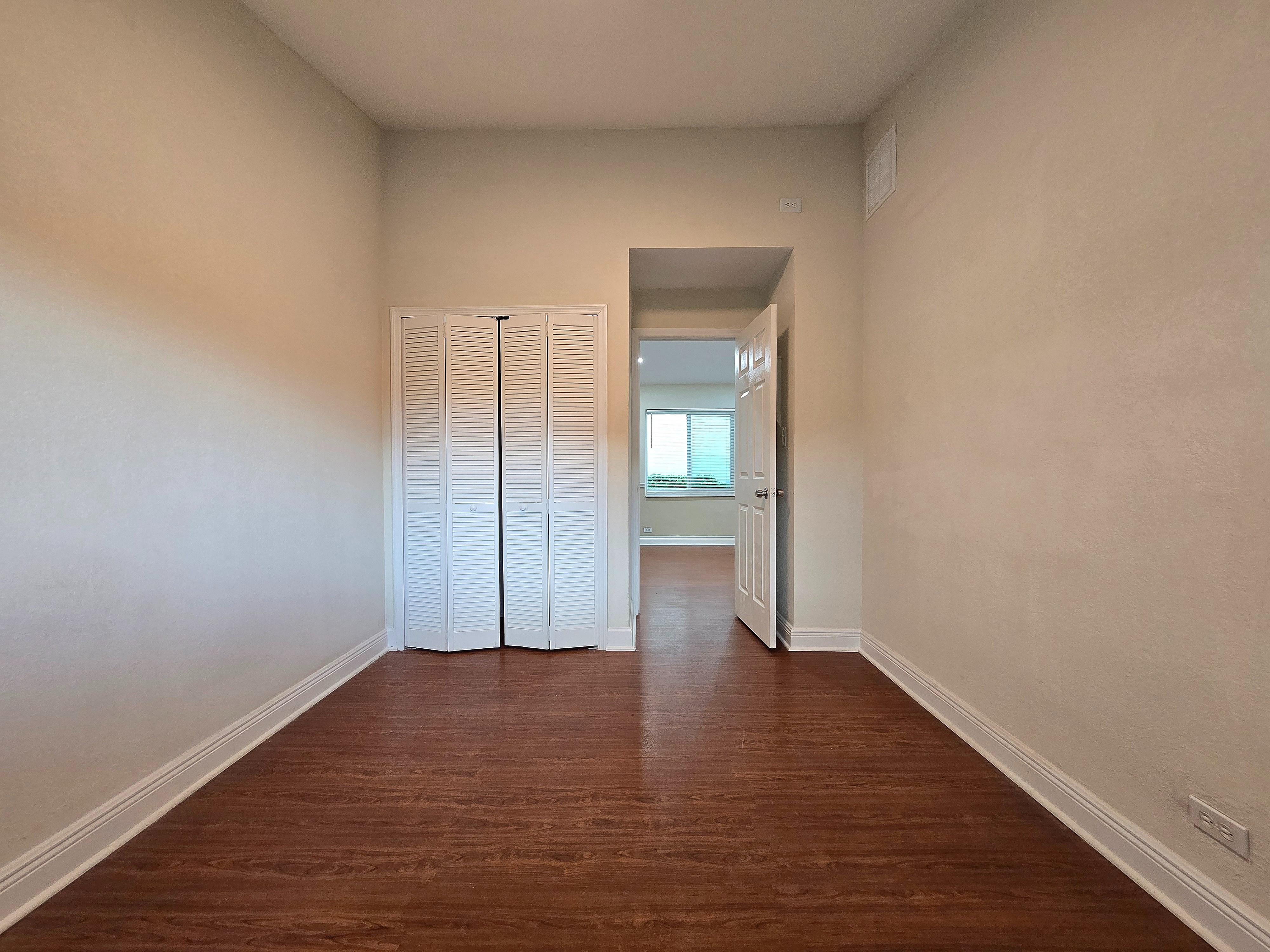 Bright and inviting hallway with elegant wooden flooring, leading to a sunlit room with large window views.