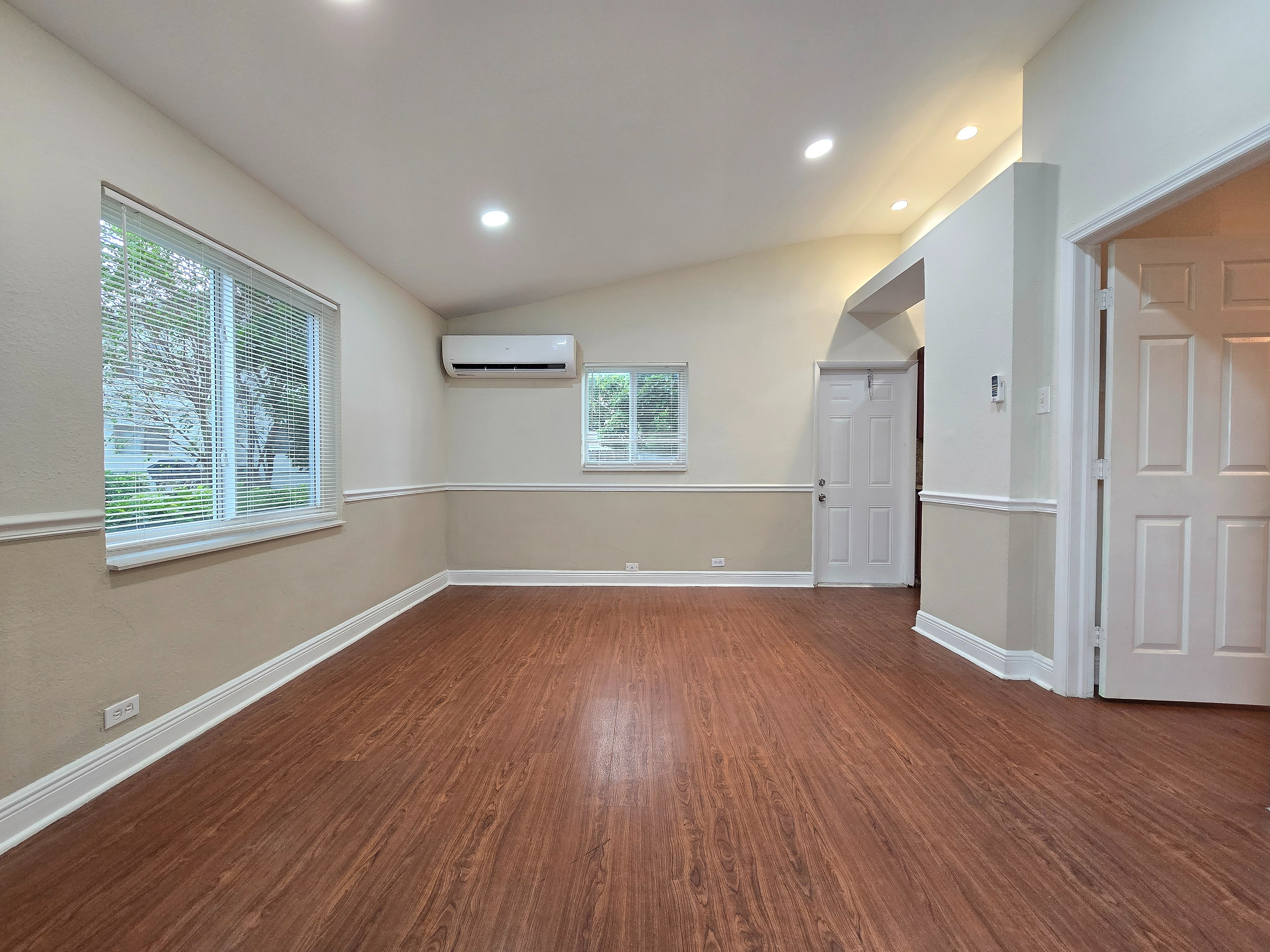 Bright and inviting living space with elegant wood flooring, ample natural light, and sleek air conditioning, perfect for comfort and relaxation.