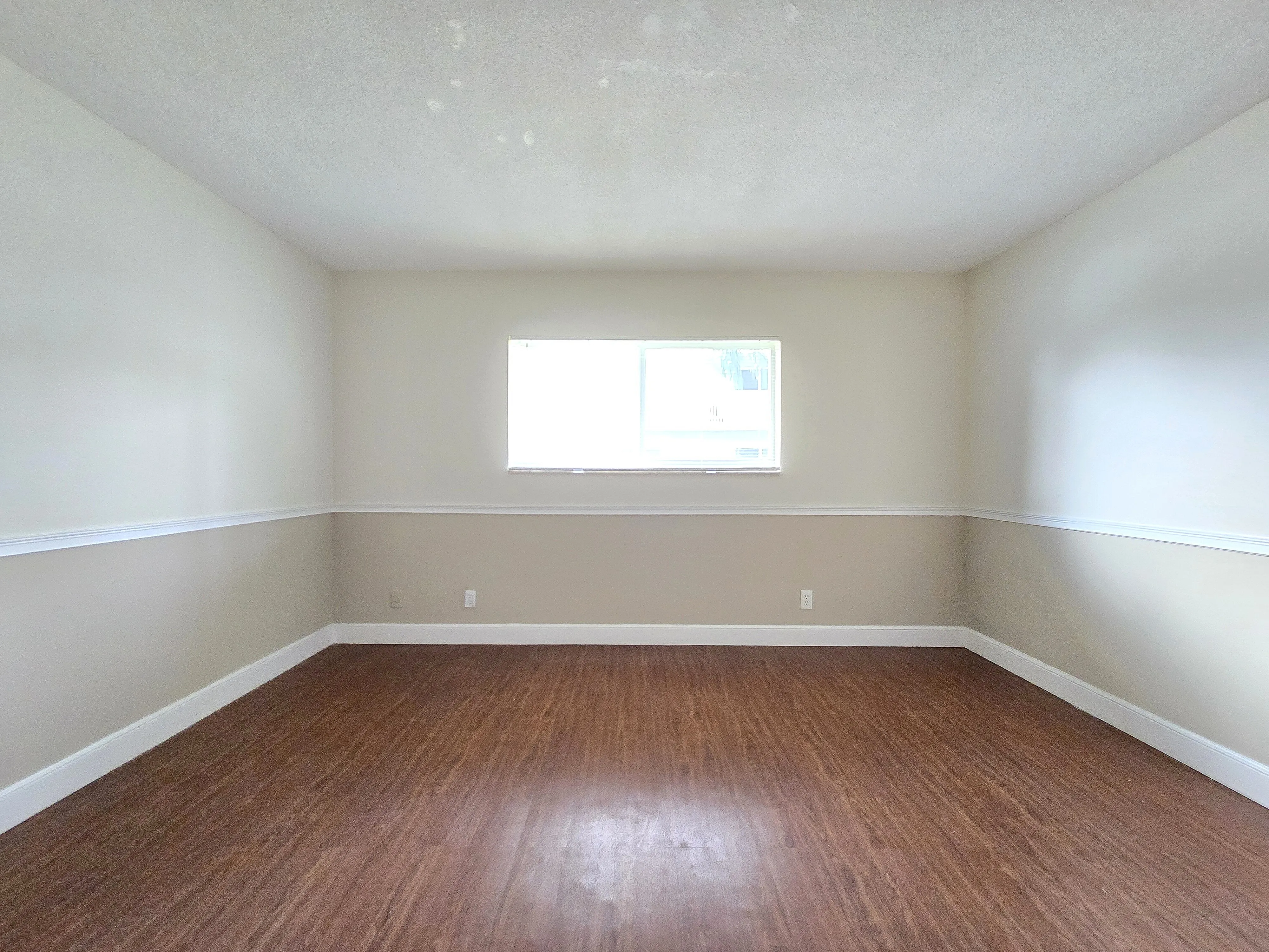 Bright and airy room with elegant wood flooring and a large window, perfect for modern living.
