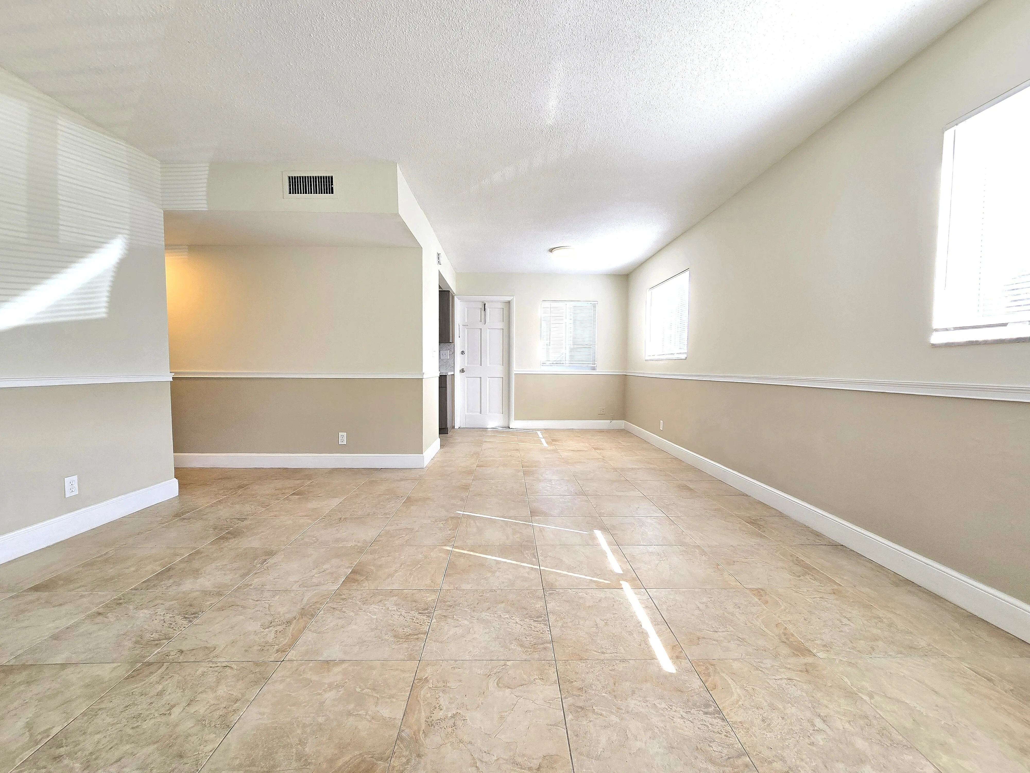 Bright and airy living space with elegant beige tile flooring and natural light streaming through multiple windows.