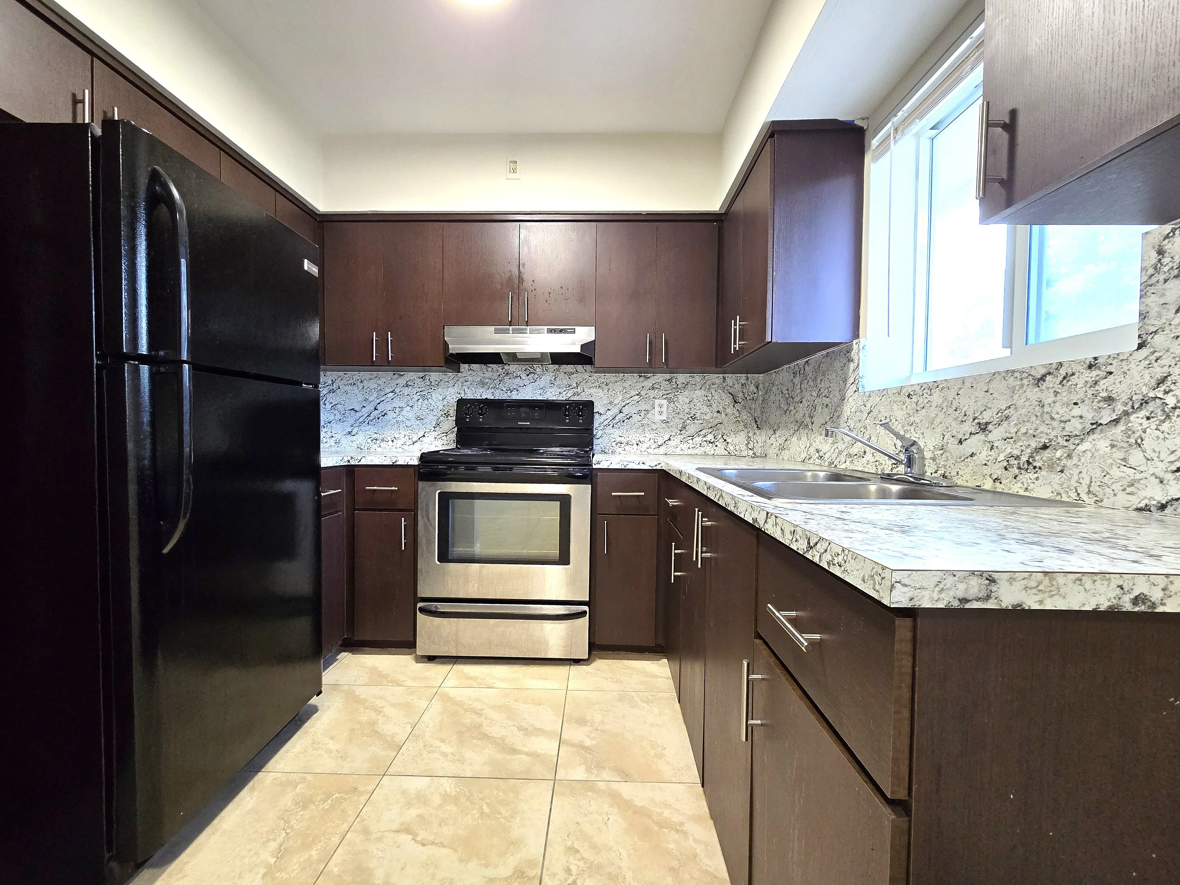 Modern kitchen with dark wood cabinets, sleek countertops, stainless steel appliances, and ample natural light from a large window.