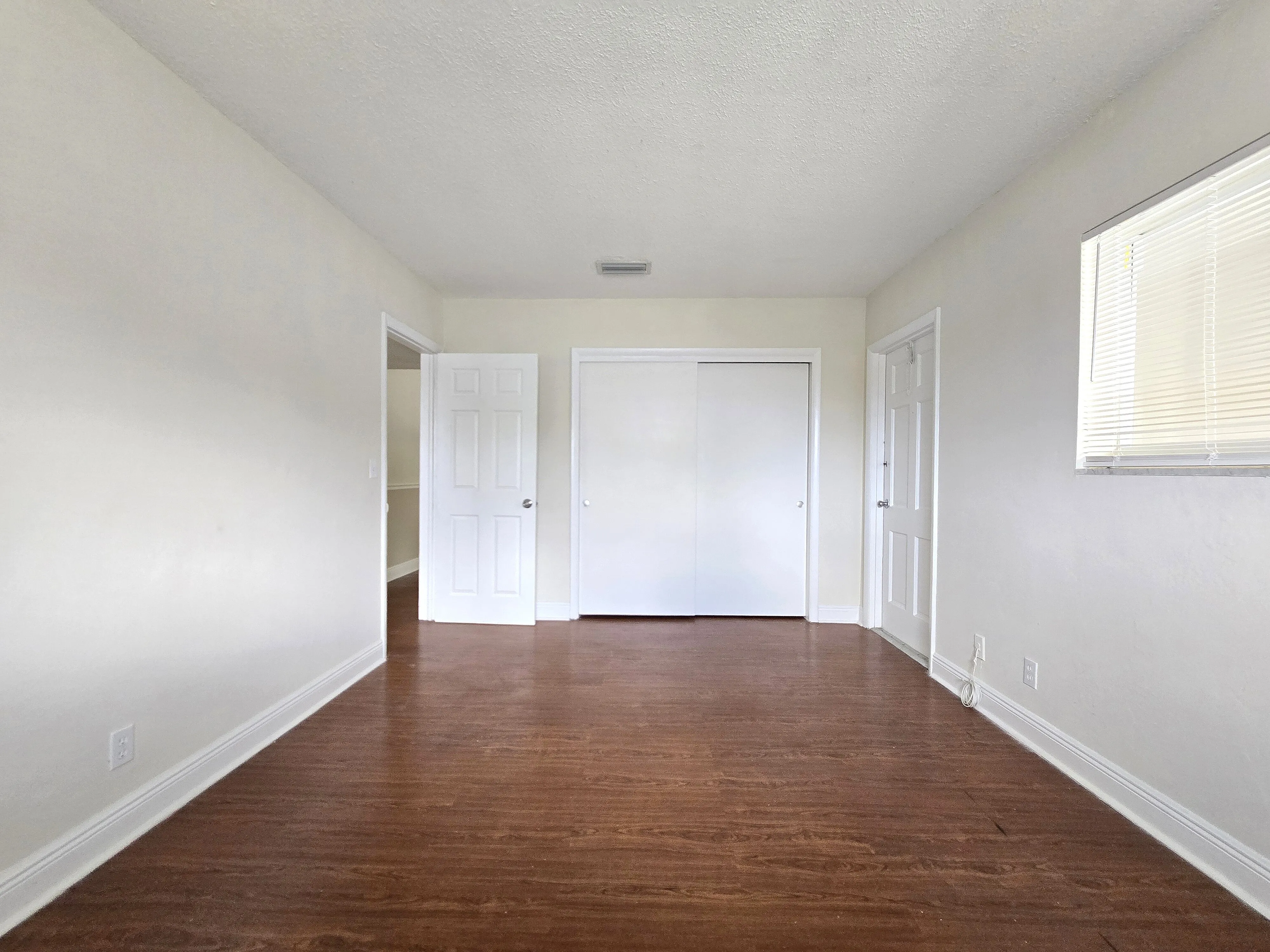 Bright and spacious empty room with hardwood floors, white walls, and ample natural light from a window, perfect for personalization.