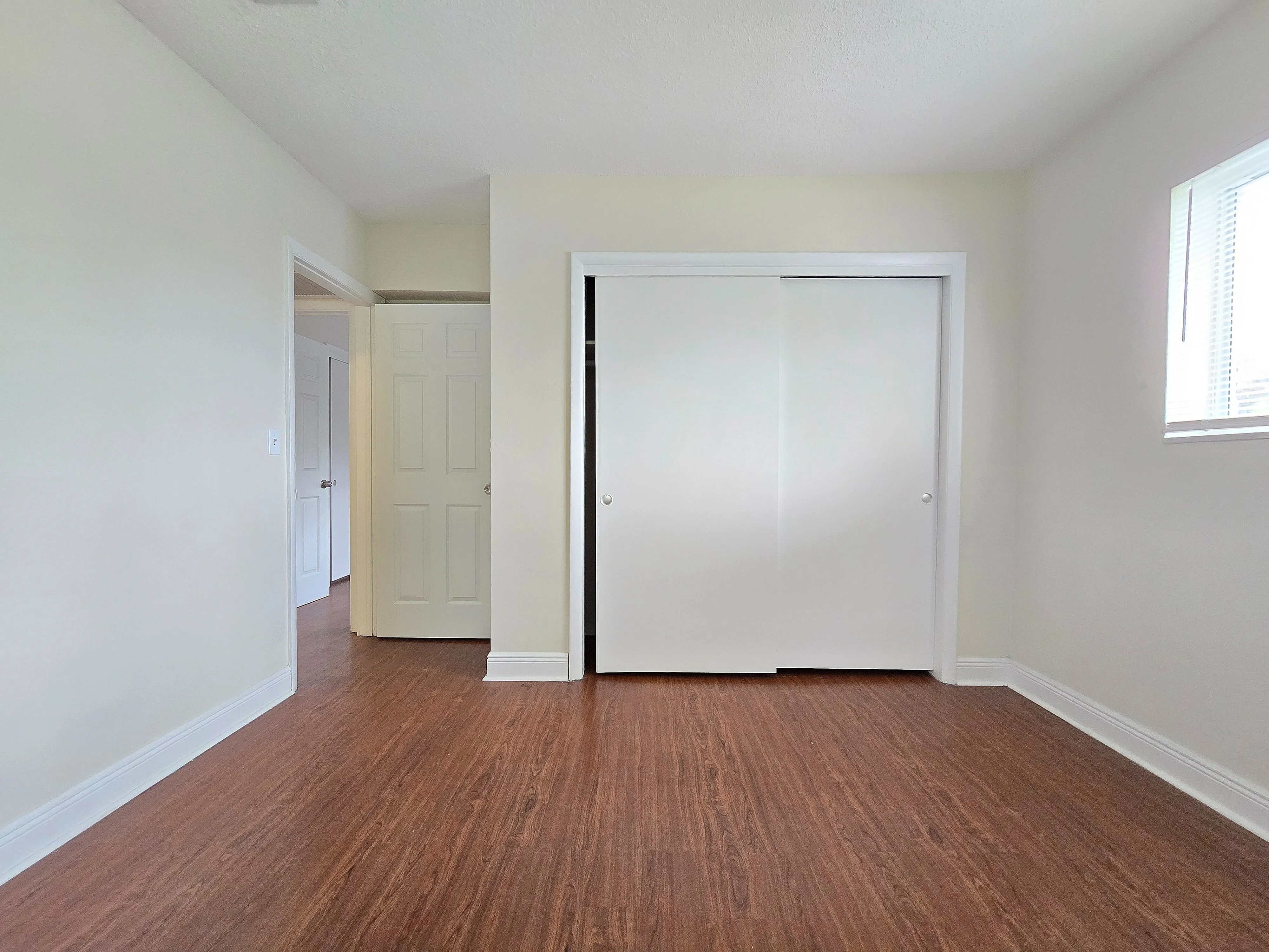 Bright and airy room featuring elegant hardwood floors, fresh white walls, and a sleek closet for ample storage.
