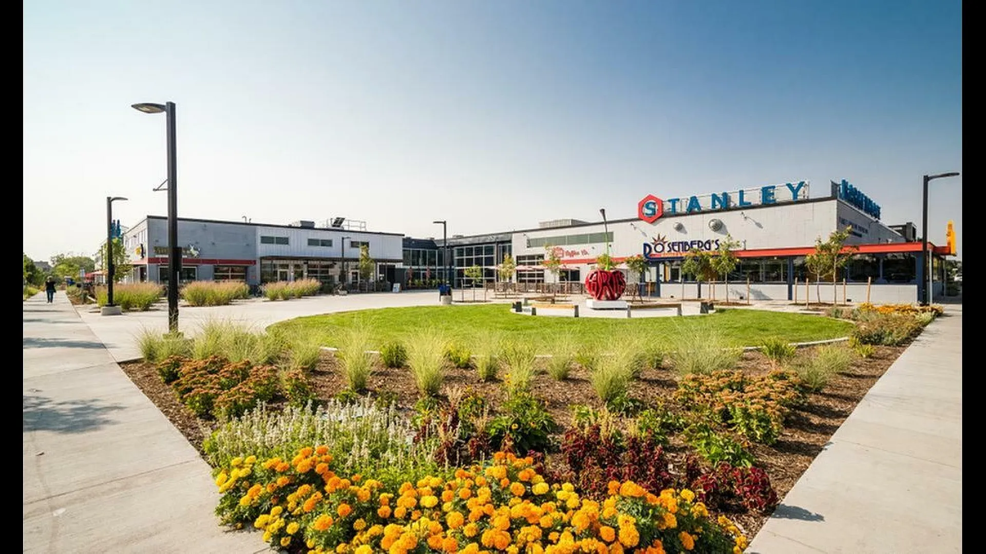 Vibrant shopping plaza with colorful flower beds, modern architecture, and inviting walkways under a clear blue sky.