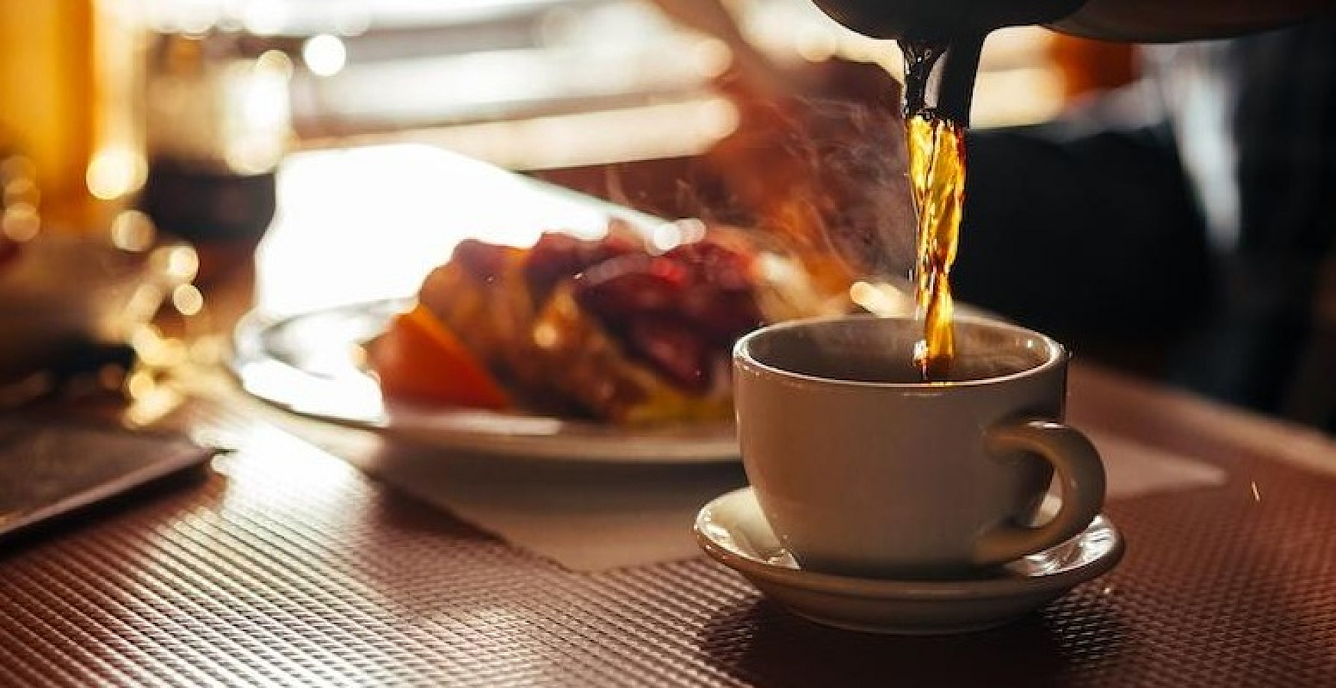 Morning ambiance with steaming coffee being poured into a cup, complemented by a delightful breakfast plate in the background.