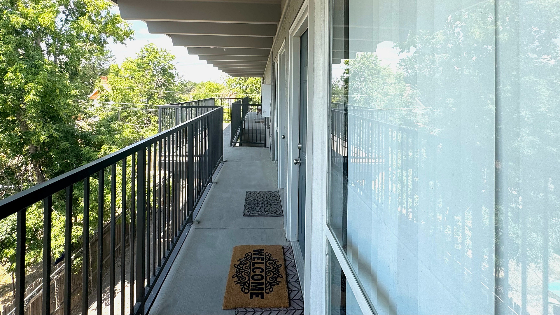 Charming apartment balcony with stylish railing, surrounded by lush greenery, inviting welcome mat, and serene outdoor views.