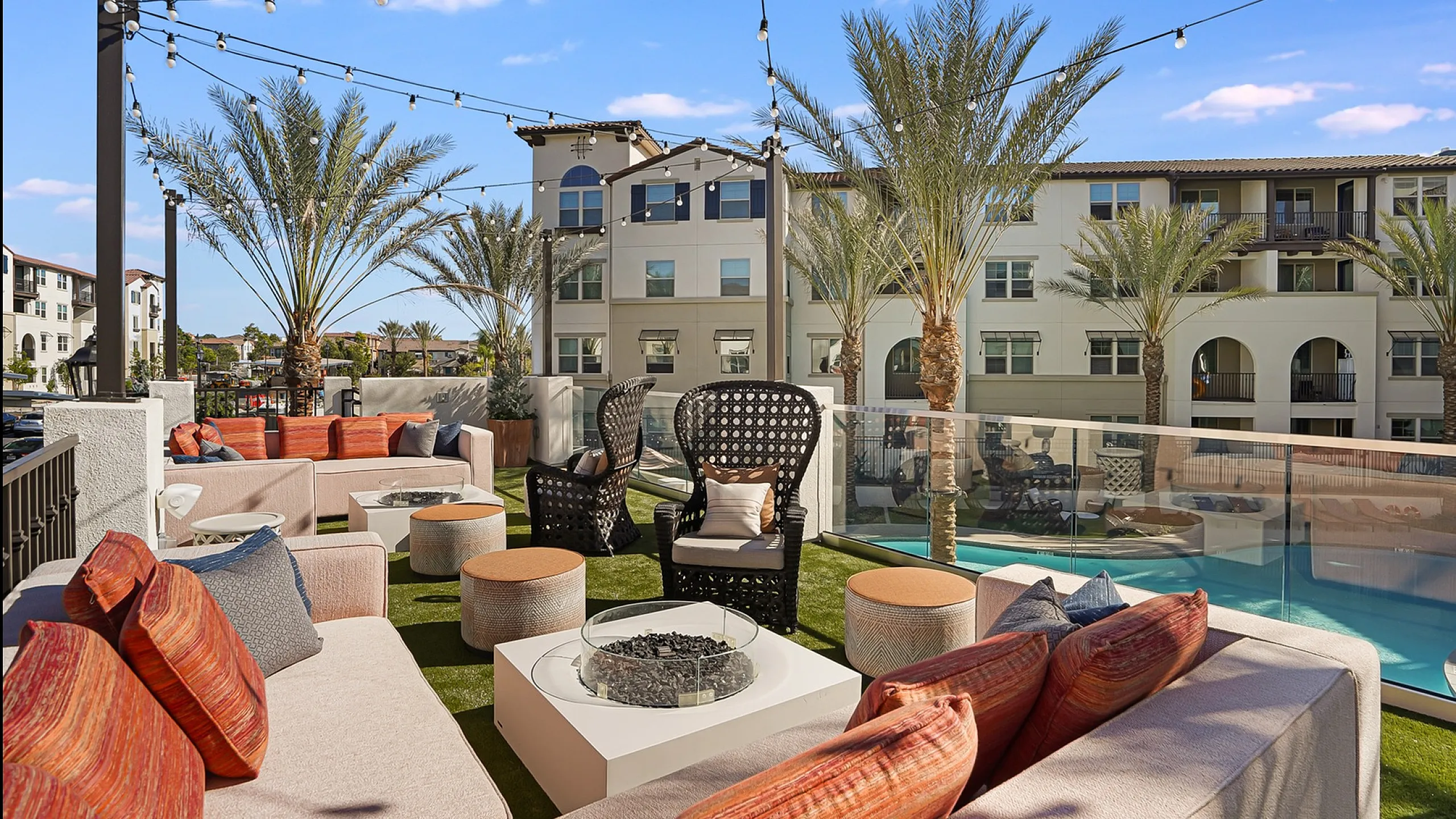 Luxurious rooftop lounge with cozy seating, palm trees, and stunning views of modern apartments and pool, perfect for relaxation and entertaining.