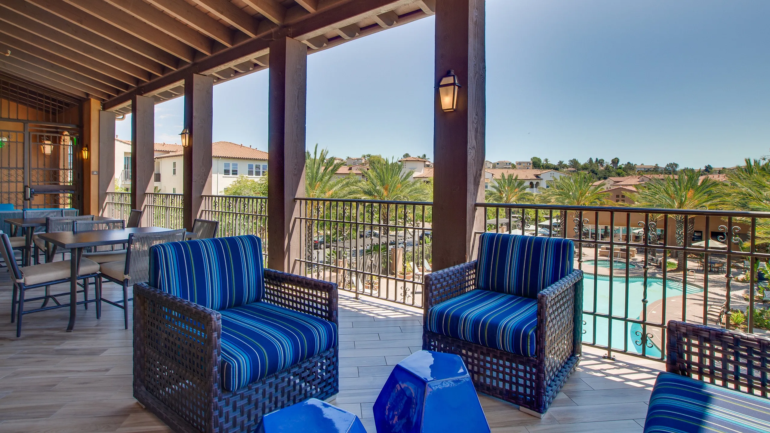 Luxurious covered balcony overlooking a sparkling pool, featuring stylish wicker seating and vibrant decor in a serene resort setting.