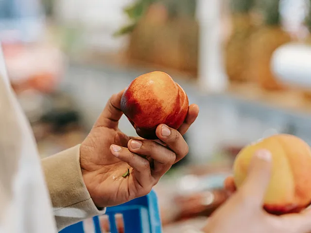 Close-up of hands holding ripe peaches in a vibrant market setting.