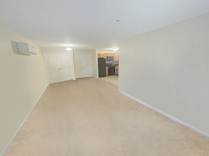 Spacious living area with plush carpeting and a modern kitchen in the background, perfect for family gatherings.