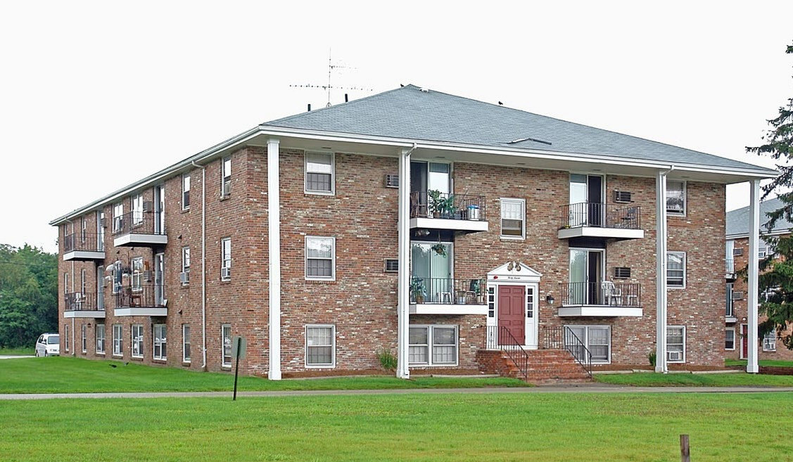 Charming red-brick apartment building with balconies and lush green surroundings, ideal for comfortable living.