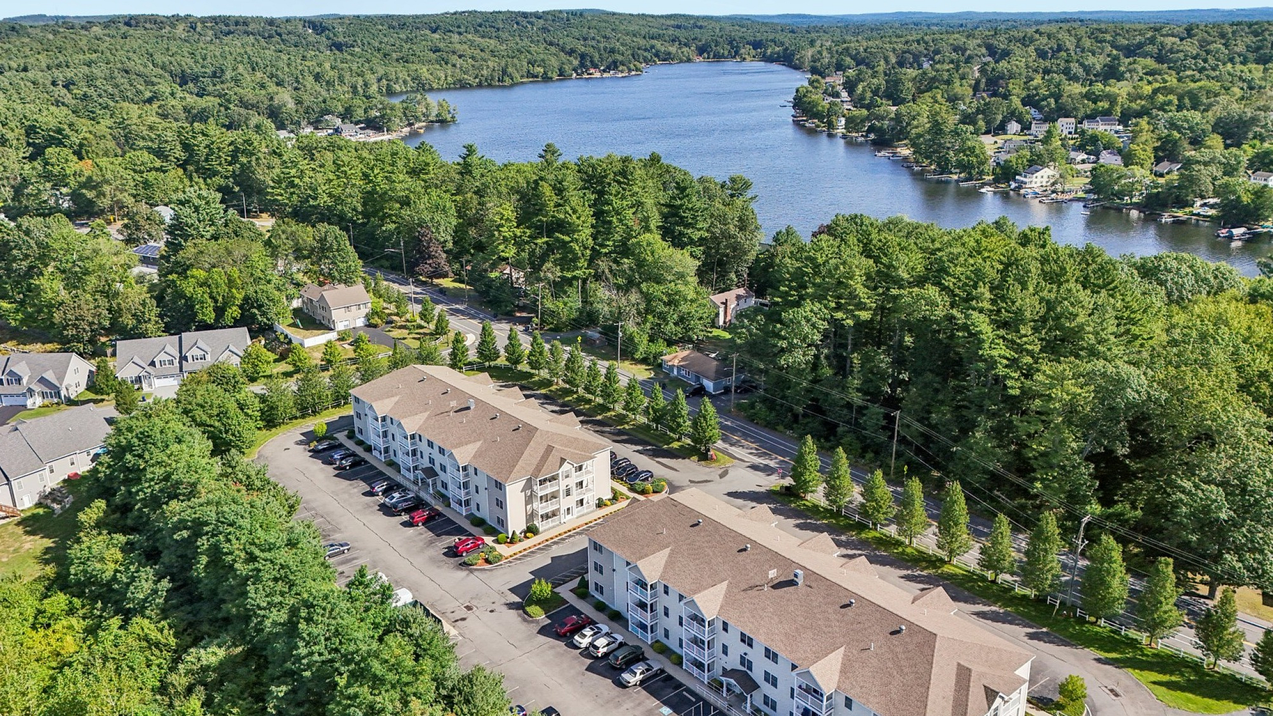 Scenic aerial view of modern apartment complex surrounded by lush greenery and picturesque lake, offering a serene and inviting living environment.