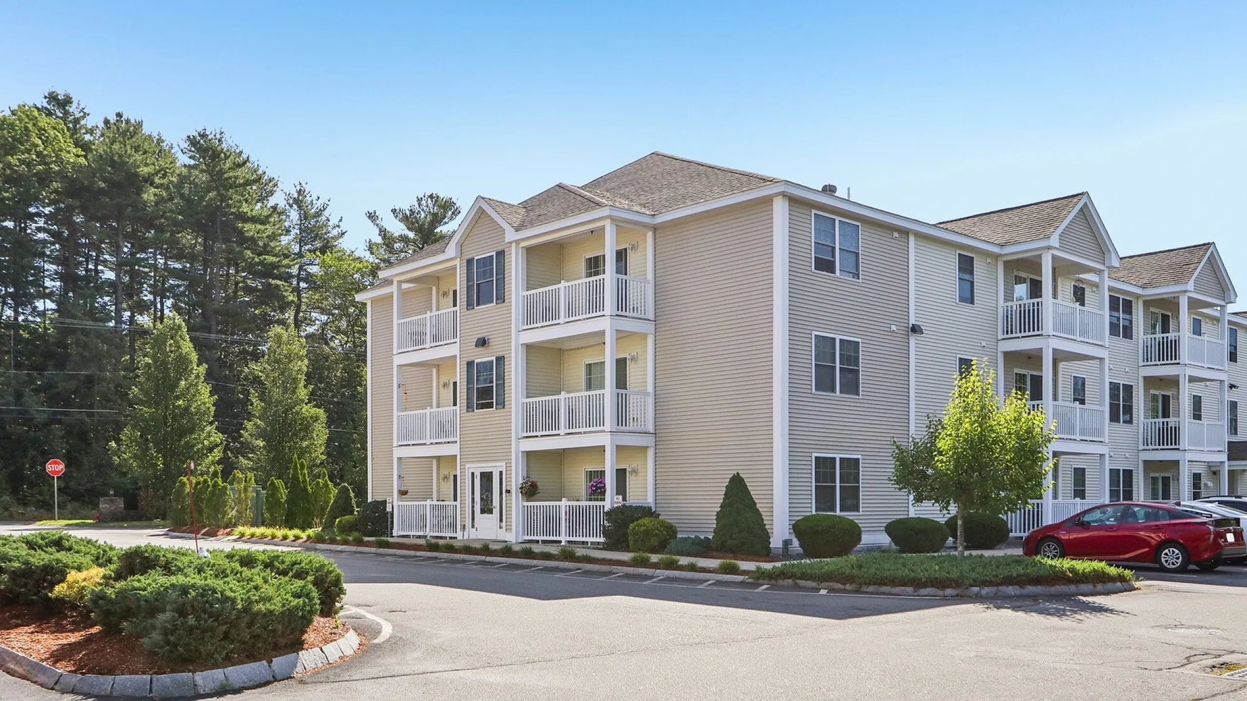 Elegant three-story apartment building with spacious balconies, surrounded by lush greenery and ample parking.