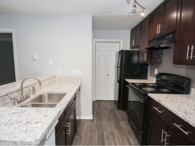 Kitchen with white granite counters, dark cabinets, wood flooring, track lighting