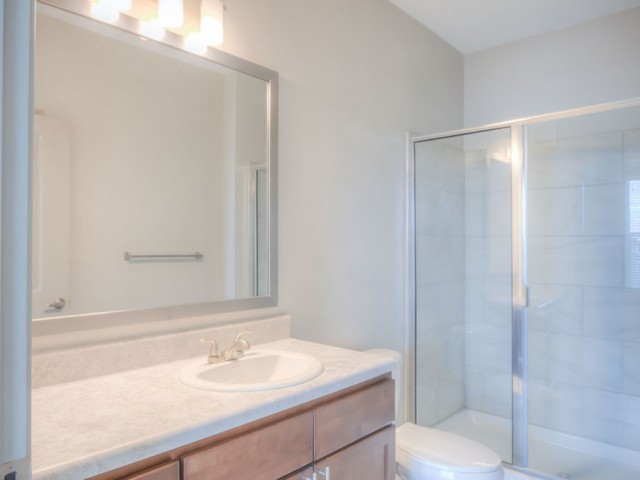 San Mateo Apartments Kissimmee Florida bathroom with walk in shower, tiled walls, large mirror with light fixture and single sink