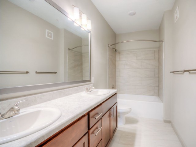 San Mateo Apartments Kissimmee Florida bathroom with double sink vanity, expansive mirror, dual lights, tub/shower combo with tile floors and tub walls