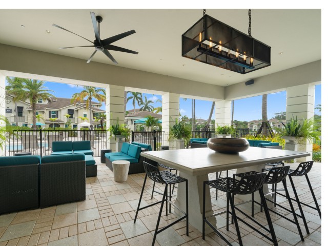 Covered open air poolside lounge with plush seating, dining table and ceiling fan