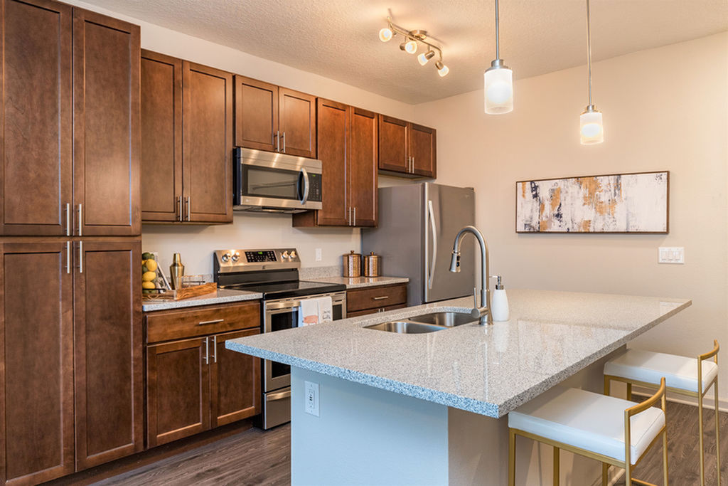 San Mateo Apartments Kissimmee Florida island kitchen with stainless steel appliances, granite counters, undermount sink in island, pendantand track lights, and vinyl plank flooring