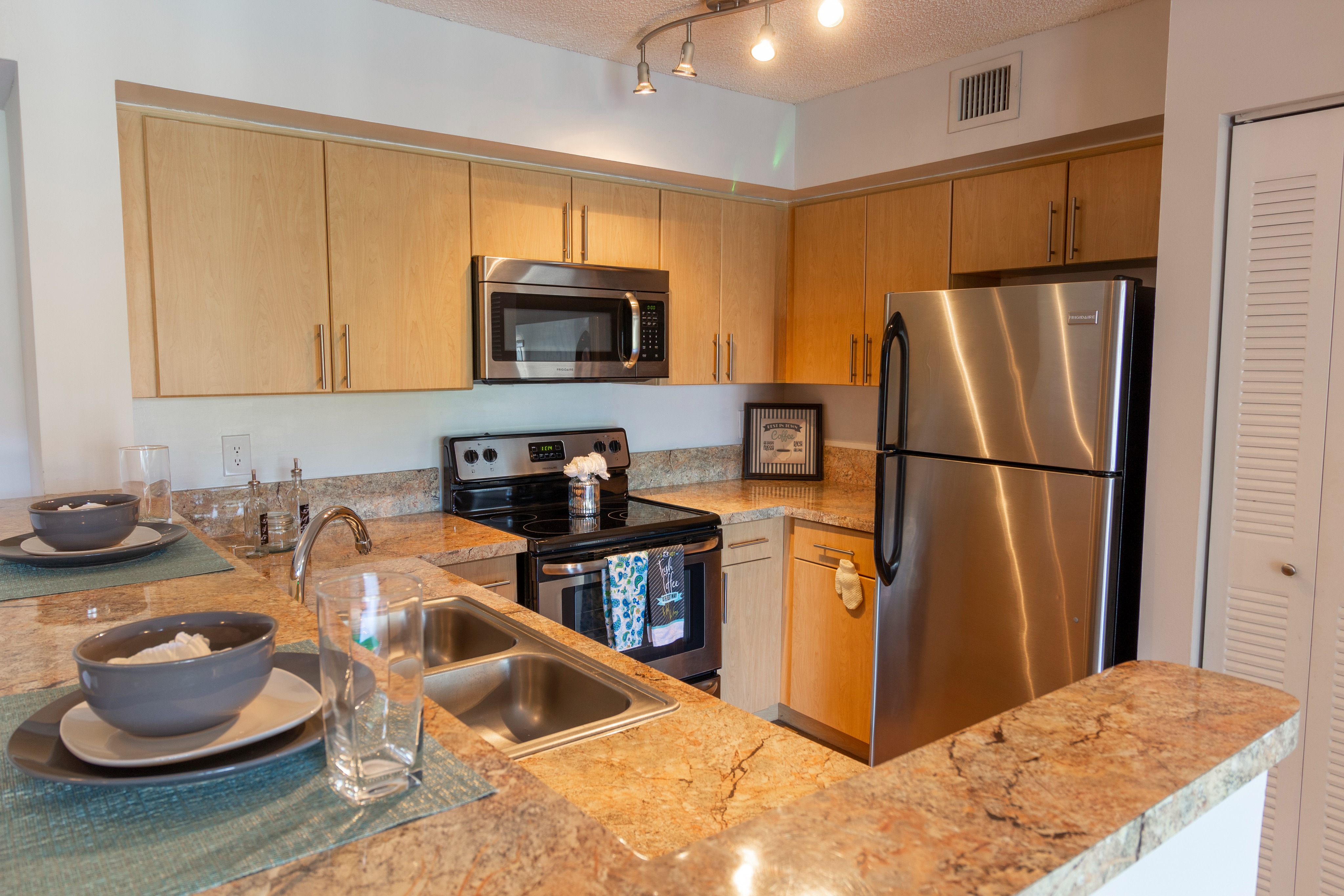 Compact kitchen counter with large stainless steel sink, overhead cabinets, and dishwasher next to double-door pantry