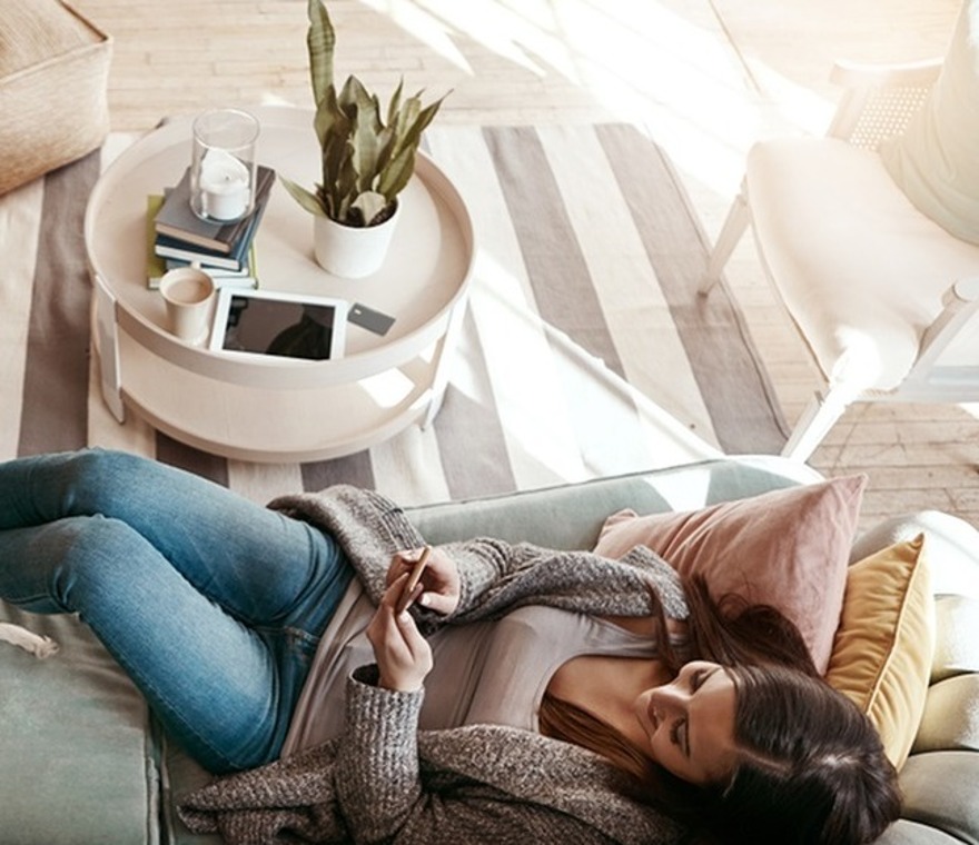 Woman laying on gray couch checking her phone