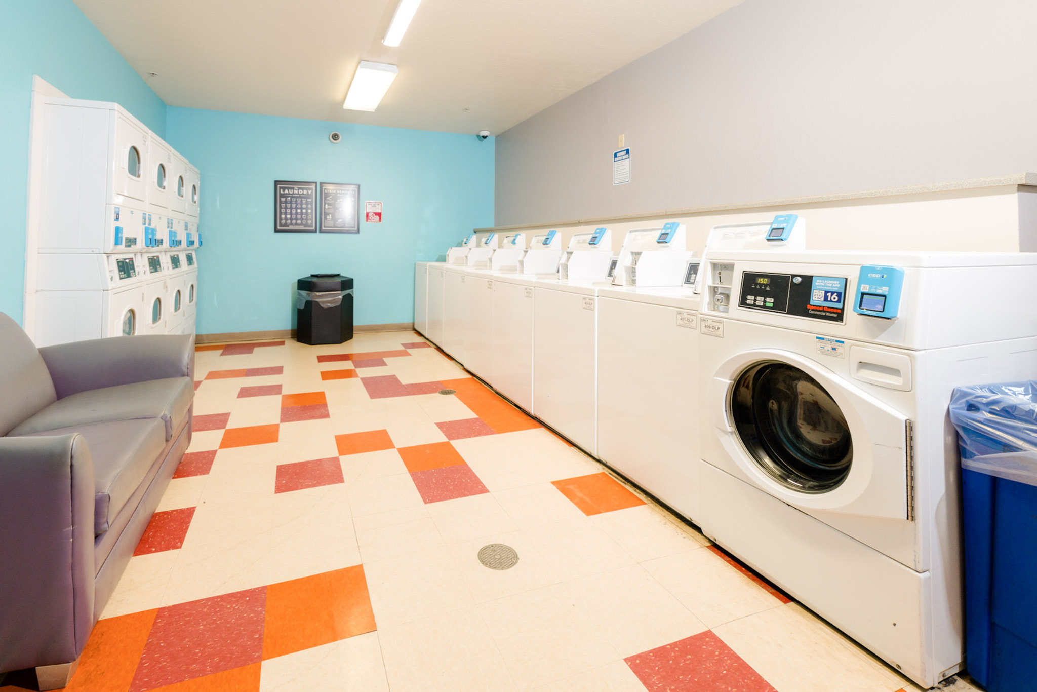 Bright and spacious laundry room equipped with modern washing machines and dryers, featuring comfortable seating and vibrant tile flooring.