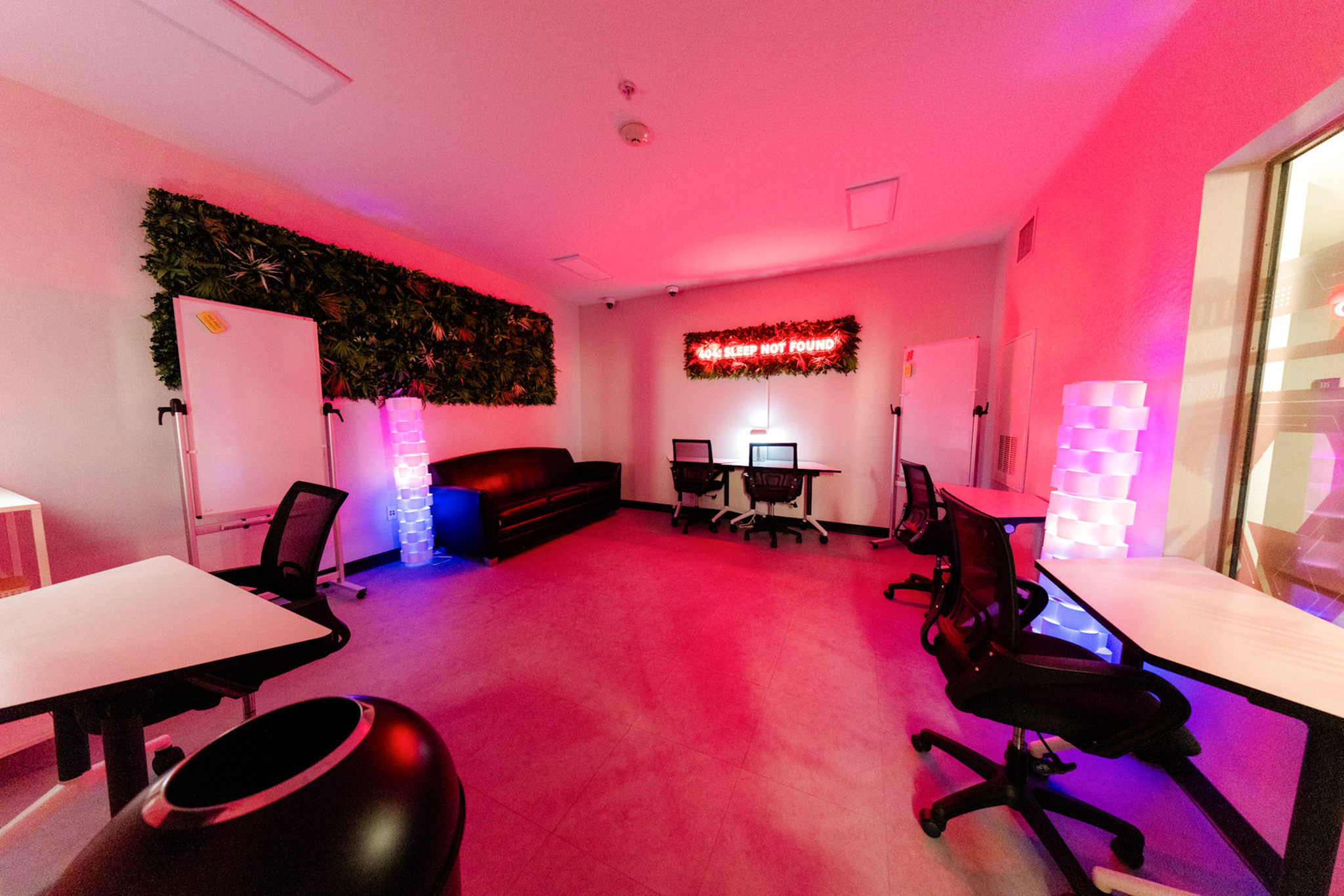 Vibrant, tech-savvy workspace featuring neon lights, modern desks, and lush green decor for a dynamic work environment.