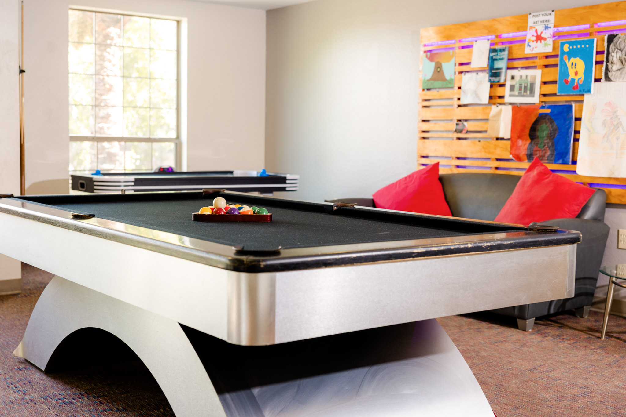 Vibrant recreation room featuring a sleek pool table with colorful billiard balls, cozy seating with plush red cushions, and eclectic wall art for a lively atmosphere.