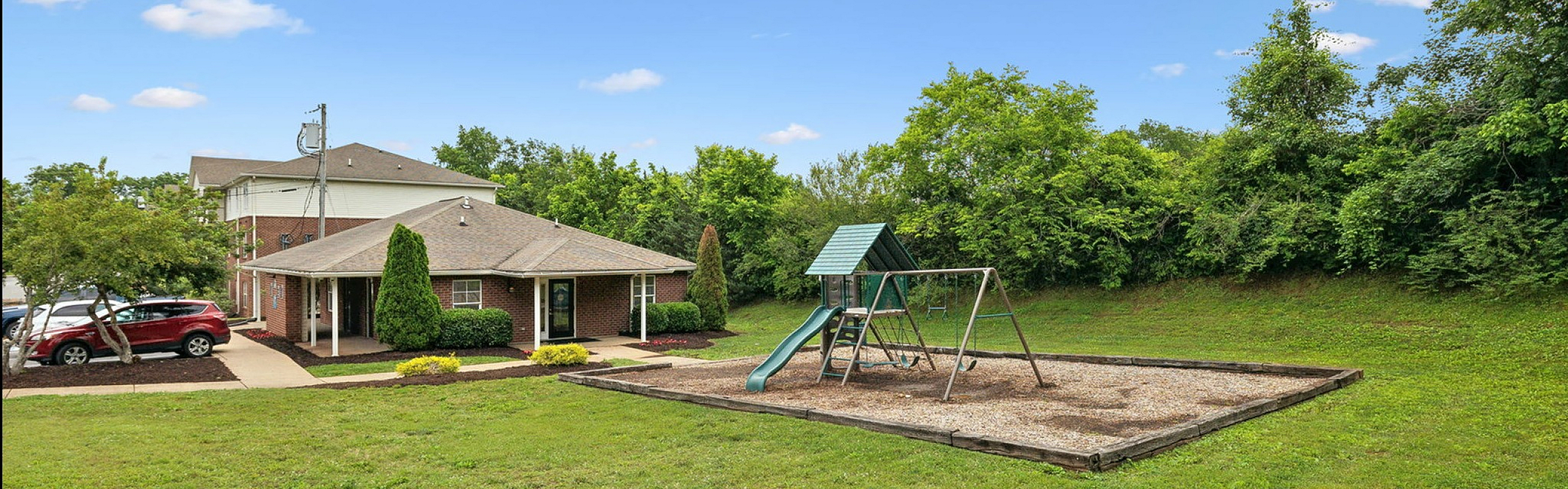 Charming apartment complex with lush green surroundings featuring a playground and modern amenities.