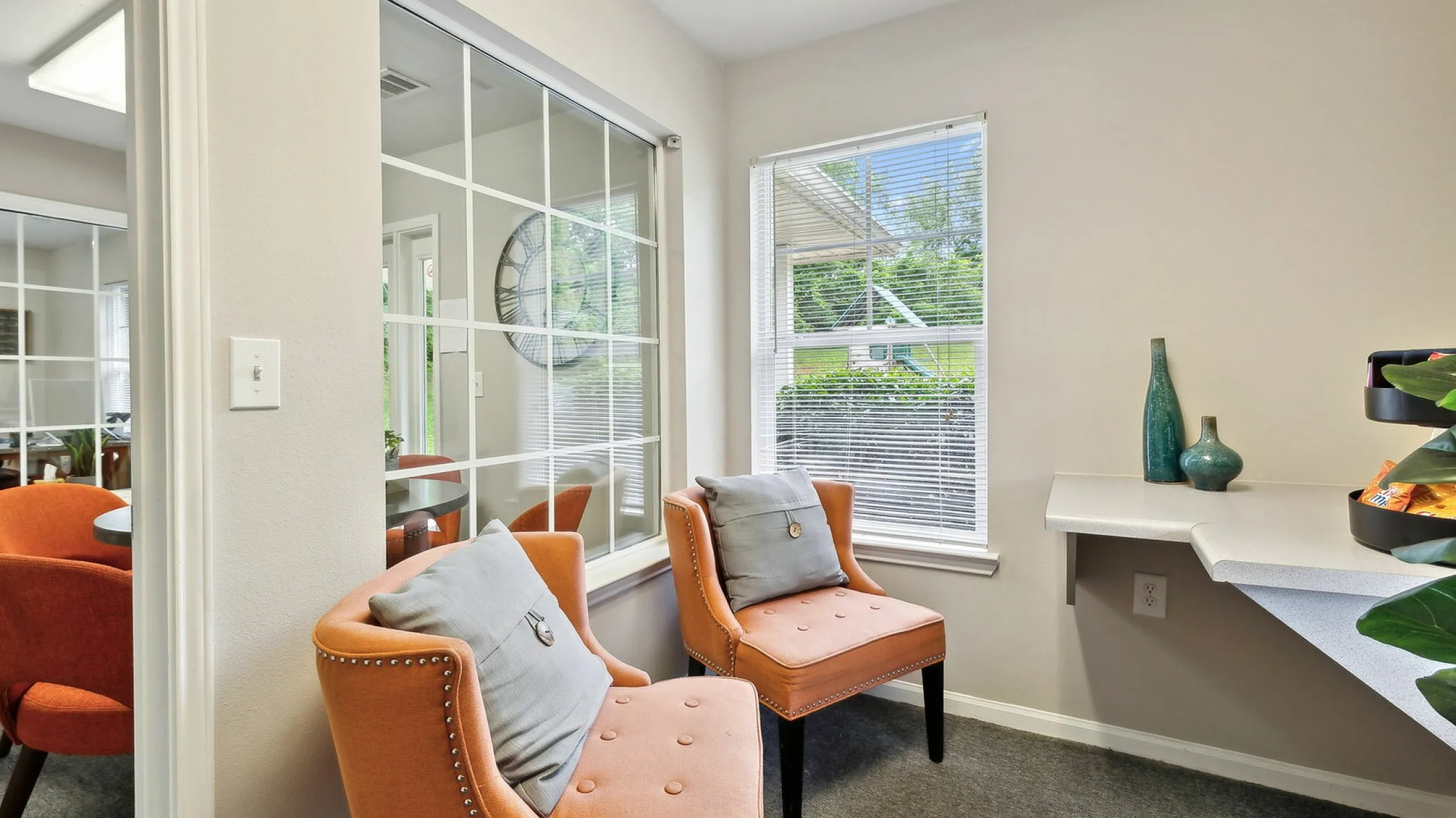 Charming seating area in modern apartment featuring two elegant orange chairs, large window with garden view, and stylish decor accents.